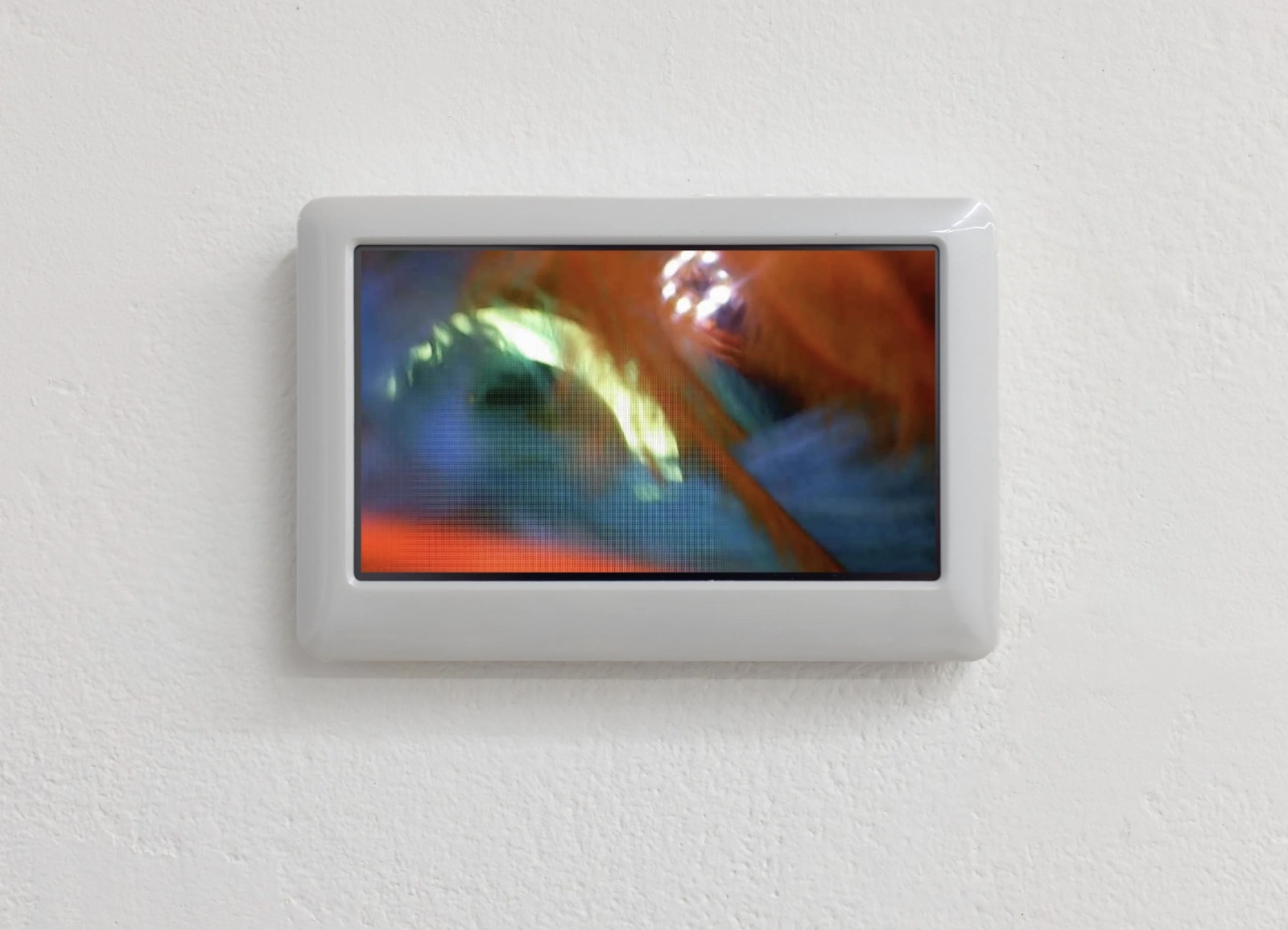 A small white-framed screen on a white wall showing blurred, saturated glare in orange, blue and green